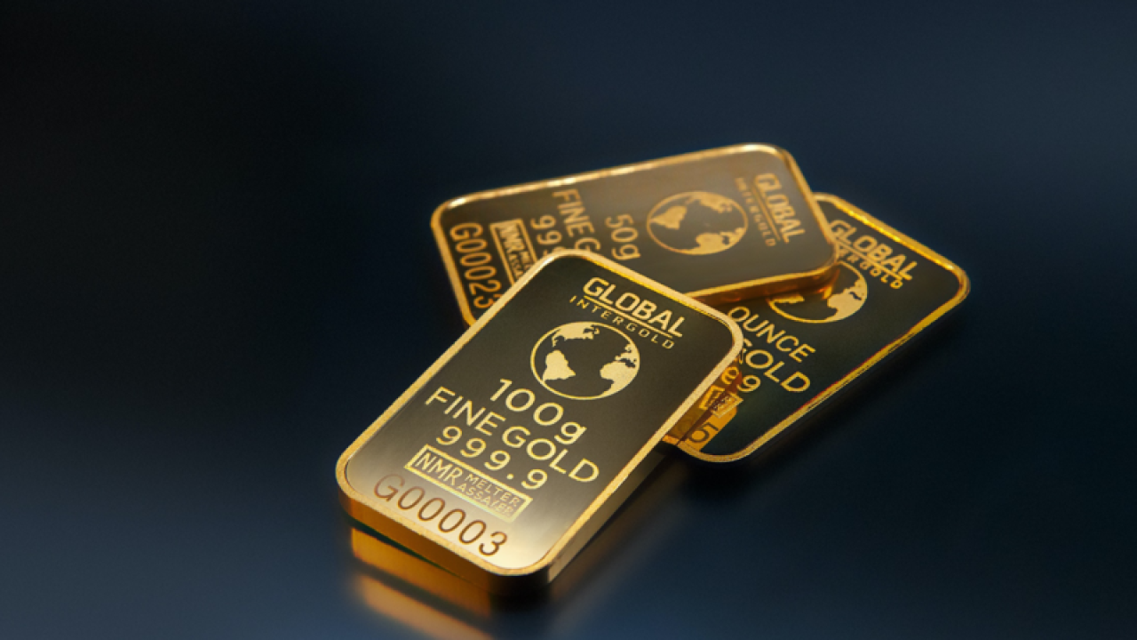 Three gold bars labeled "GLOBAL INTERGOLD" are displayed, offering a gleaming testament to inflation protection. The front bar is marked "100g FINE GOLD 999.9," while the other two are labeled "50g" and "1 ounce." Their reflective, shiny surfaces stand out against the dark background. | MONEY6X
