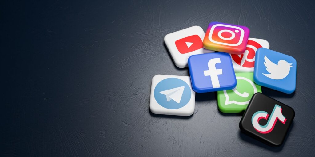 A dark surface is scattered with various social media application icons, including YouTube, Instagram, Pinterest, WhatsApp, Facebook, Twitter, Telegram, and TikTok. The colorful icons create a contrast against the minimalistic background—highlighting some of the best social media to make money. | MONEY6X