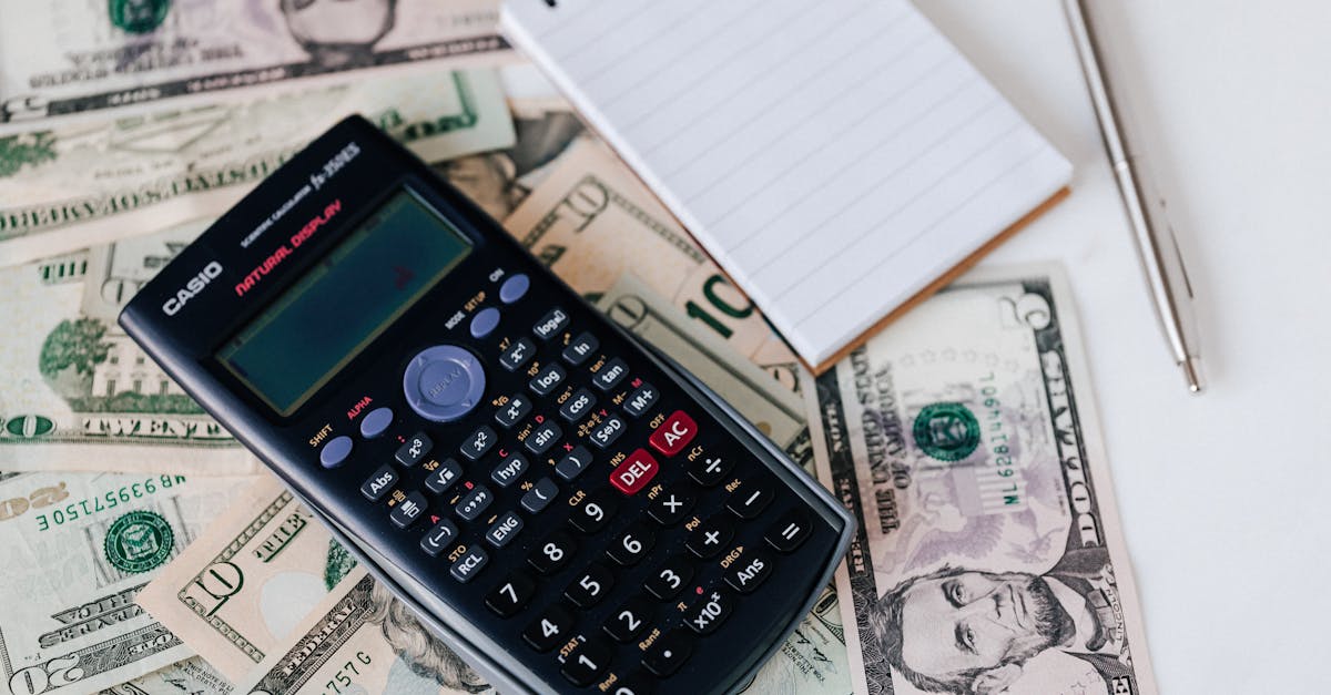 A scientific calculator rests on spread-out US dollar bills, including ten, twenty, and five-dollar notes. To the right of the calculator is a small notepad with a pen placed on top of it, possibly tallying up expenses or calculating a strategy for improving that crucial credit score. | MONEY6X