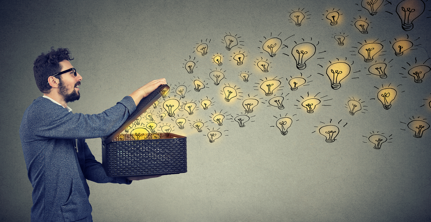 A man with glasses and a beard opens a black woven box, releasing numerous glowing lightbulb illustrations that float away. The background is a muted gray, and the lightbulbs create a sense of creativity and nonprofit fundraising ideas emerging from the box. | MONEY6X