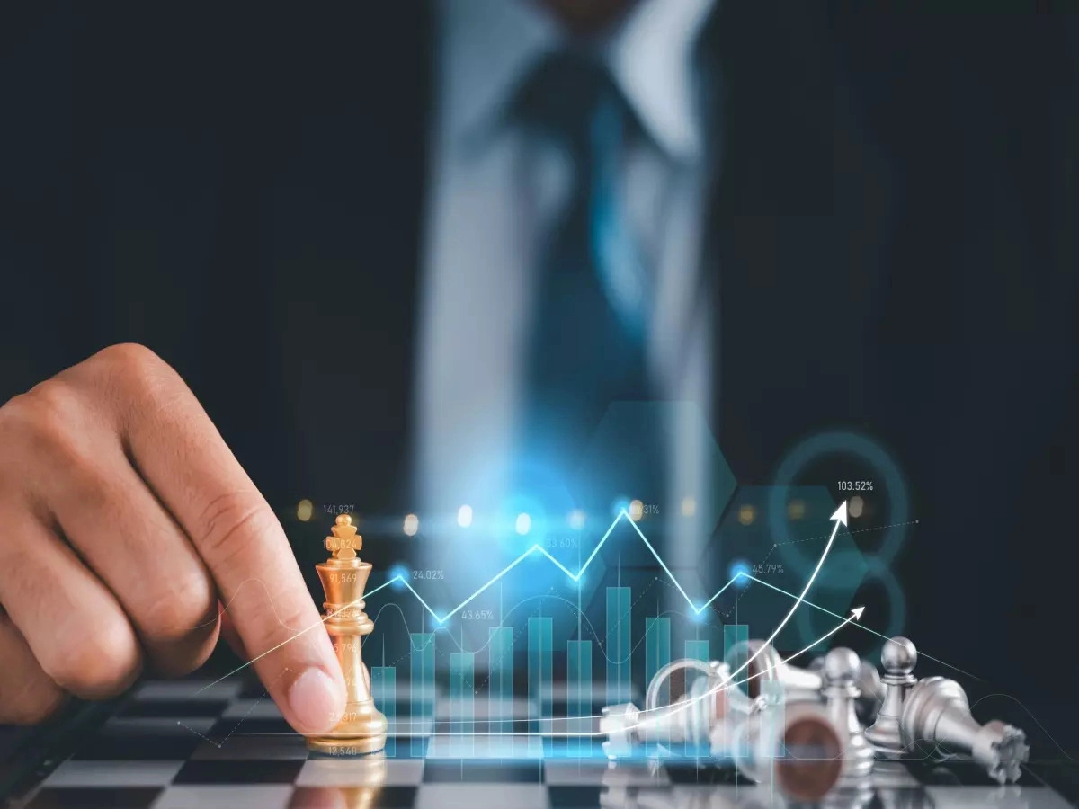 A person in a suit moves a golden chess piece on a chessboard. Silver pieces are toppled over. A transparent graph with rising arrows and bar charts overlays the image, suggesting strategic planning or financial growth, much like the careful strategy required in investing. | MONEY6X