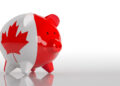 A piggy bank painted with the Canadian flag, featuring a red maple leaf and red sides, is placed on a reflective white surface with a plain white background. | MONEY6X