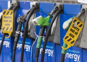 Four gas pumps at a station, with some nozzles covered by yellow “Sorry out of use” signs, indicating they are not available for fueling. The pumps are blue and display the word “synergy.”. | MONEY6X