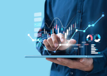 A person using a tablet with their finger touching the screen. Various digital graphs, charts, and data visualizations appear to be floating above the tablet, indicating they are analyzing complex data such as what are unit investment trusts. The background is a solid light blue. | MONEY6X