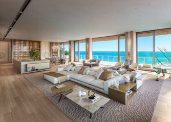 A spacious, modern living room with beige and neutral tones features plush seating, large windows offering a stunning ocean view, wooden flooring, a contemporary kitchen with a wine display, and a stylish dining area. Considering selling your home quickly? This space opens to a balcony with outdoor seating. | MONEY6X