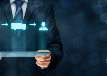 A person in a suit and tie holds a digital tablet. Above the tablet, holographic icons representing online shopping, dropshipping, and delivery are displayed, connected by arrows. The background is dark with blurred, glowing circles. | MONEY6X