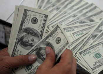 A person is handling a large number of U.S. 100-dollar bills, fanning them out on a table. The image shows a close-up of the hands counting the money, with the bills clearly visible and arranged in a spread, making one ponder, "How can I make $100 a day everyday? | MONEY6X
