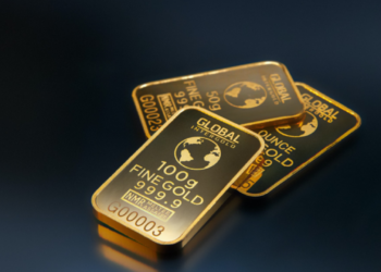 Three gold bars labeled "GLOBAL INTERGOLD" are displayed, offering a gleaming testament to inflation protection. The front bar is marked "100g FINE GOLD 999.9," while the other two are labeled "50g" and "1 ounce." Their reflective, shiny surfaces stand out against the dark background. | MONEY6X