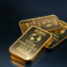 Three gold bars labeled "GLOBAL INTERGOLD" are displayed, offering a gleaming testament to inflation protection. The front bar is marked "100g FINE GOLD 999.9," while the other two are labeled "50g" and "1 ounce." Their reflective, shiny surfaces stand out against the dark background. | MONEY6X