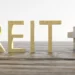The image displays the word "REITs" formed with golden 3D letters, placed on a wooden surface. To the left of the text is a miniature house, and to the right is a structure made of white cube-shaped blocks with a golden house-shaped block at the top. | MONEY6X