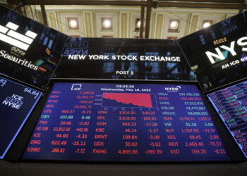 Electronic screens at the New York Stock Exchange display various stock prices, changes, and indexes. The central screen shows a large downward trend, with red numbers signifying losses across multiple sectors. The time and date are also visible: 3:23:39 on Wednesday, May 18, 2022. Investing in stocks appears challenging today. | MONEY6X