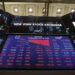 Electronic screens at the New York Stock Exchange display various stock prices, changes, and indexes. The central screen shows a large downward trend, with red numbers signifying losses across multiple sectors. The time and date are also visible: 3:23:39 on Wednesday, May 18, 2022. Investing in stocks appears challenging today. | MONEY6X