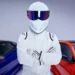 A person wearing a full white racing suit and helmet with a reflective visor stands with arms crossed. Behind them are two sports cars, one blue and one red, in a well-lit studio, demonstrating how you can convey style and charisma without showing your face on platforms like OnlyFans. | MONEY6X