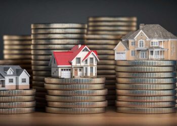 Three miniature houses sit atop stacks of coins of varying heights. The houses are detailed, with the first featuring a blue roof, the second with a red roof, and the third with a beige roof. The image symbolizes the concept of real estate investment and money in 6x REIT holdings. | MONEY6X