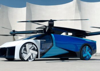 A sleek futuristic blue and white flying car with four large propellers on top, parked in front of a modern white building with curved architectural elements. Investors eyeing flying car stocks are excited by its streamlined design and large wheels, combining features of both a car and a drone. | MONEY6X