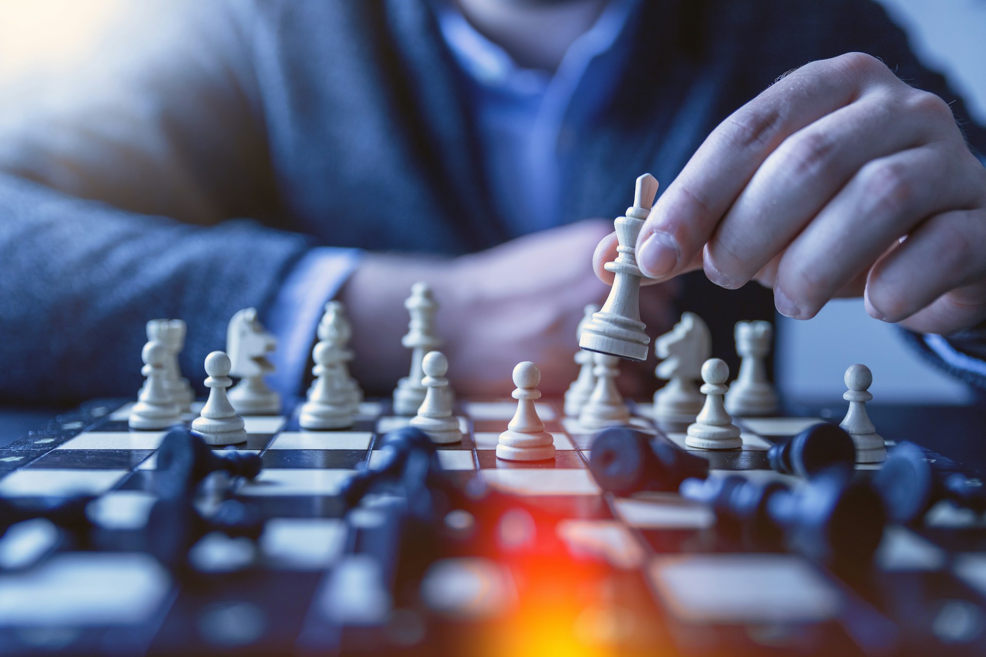 A person in a suit is playing chess, holding a white knight piece above a chessboard. Various chess pieces are scattered across the board. The focus is on the player's hand and the white knight piece, indicating strategic earning strategies in progress. | MONEY6X