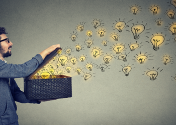 A man with glasses and a beard opens a black woven box, releasing numerous glowing lightbulb illustrations that float away. The background is a muted gray, and the lightbulbs create a sense of creativity and nonprofit fundraising ideas emerging from the box. | MONEY6X