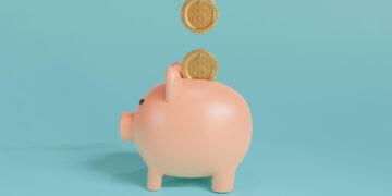 A light pink piggy bank is positioned on a light blue background. Two golden coins, each with a dollar sign, appear to be falling into the slot at the top of the piggy bank, suggesting the act of saving money efficiently with Money6x.com Save Money. | MONEY6X