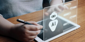 A person is holding a stylus pen, interacting with a transparent digital interface on a tablet. The interface displays an AI icon and speech bubbles, suggesting a chat with artificial intelligence to improve your financial literacy. | MONEY6X
