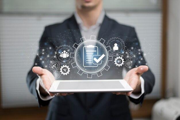 A person in a suit holds a tablet. Above it, digital icons depict gears, people, and a clipboard with a checkmark, symbolizing process management or task completion in a business setting. | MONEY6X