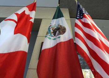 Flags of Canada, Mexico, and the United States are displayed side by side. The Canadian flag features a red maple leaf, the Mexican flag shows an eagle with a snake, and the American flag has stars and stripes, symbolizing unity amid past disputes like the Trump tariffs. | MONEY6X