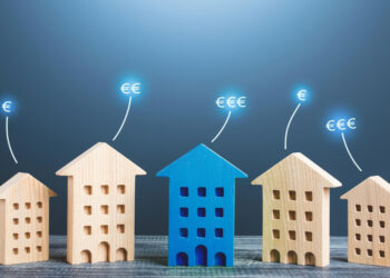 Five wooden house models stand in a row on a table, with the central house painted blue. Euro symbols (€) float above each house, representing housing prices or real estate value—ideal for illustrating passive income opportunities. Blue gradient background. | MONEY6X