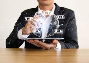 A person in a suit uses a tablet, with a transparent globe and digital currency symbols superimposed, representing global finance, technology, and the rise of online income opportunities. | MONEY6X