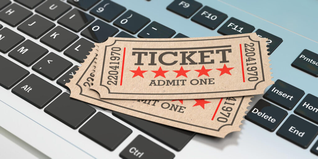 Two vintage-style admission tickets with red stars and "TICKET ADMIT ONE" text rest on a computer keyboard, suggesting online ticket purchasing or booking, ideal for securing memberships and seasonal passes. | MONEY6X