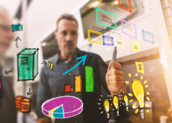 A person draws colorful business charts, diagrams, and lightbulbs on a transparent board, planning strategies, with another person’s reflection visible in the background. | MONEY6X