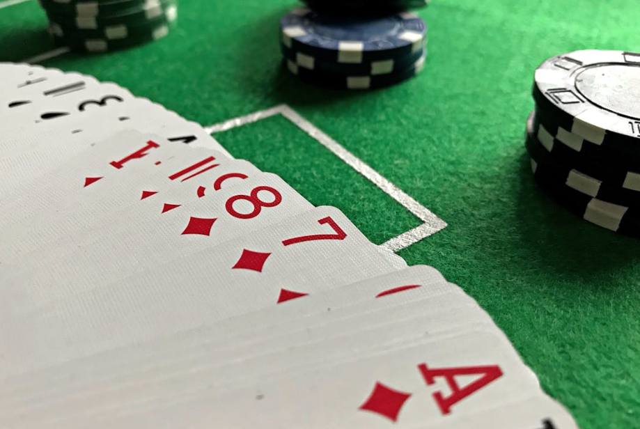 A close-up view of playing cards spread out on a green casino table, showing a sequence of diamonds. Stacks of poker chips in black, white, and blue are visible in the background. | MONEY6X