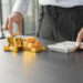 A person in business attire stacks gold coins and bars on a desk while using a calculator, suggesting financial planning or investment in gold. | MONEY6X