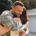 A man in military uniform smiles warmly as he hugs a woman outdoors, in front of a garage, during the daytime. | MONEY6X