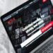 A laptop displaying the Netflix homepage with the message “Unlimited movies, TV shows, and more,” resting on a white bedspread. The Netflix logo and various show thumbnails are visible on the screen. | MONEY6X