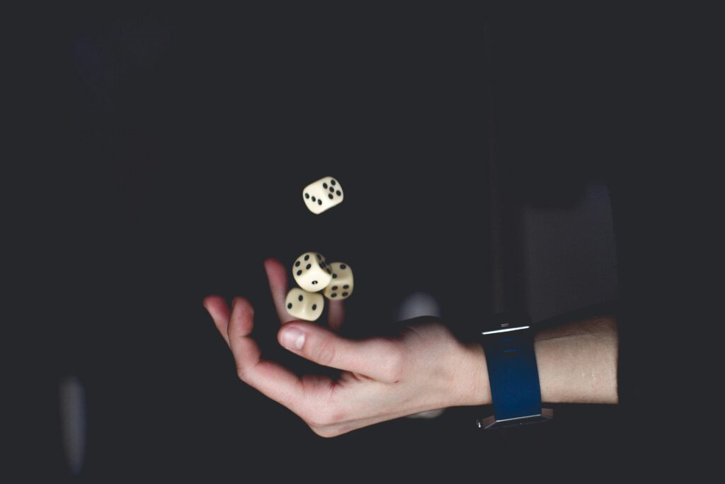 A hand wearing a blue watch tosses four white dice in the air against a dark background, evoking the importance of bankroll management in games of chance. | MONEY6X