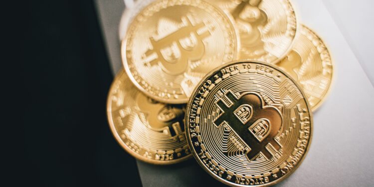 Several shiny gold Bitcoin coins with the Bitcoin symbol are stacked on a laptop keyboard, emphasizing the concept of digital currency and cryptocurrency technology. | MONEY6X