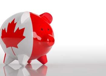A piggy bank painted with the Canadian flag, featuring a red maple leaf and red sides, is placed on a reflective white surface with a plain white background. | MONEY6X