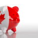 A piggy bank painted with the Canadian flag, featuring a red maple leaf and red sides, is placed on a reflective white surface with a plain white background. | MONEY6X
