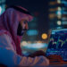 A man in traditional Middle Eastern attire analyzes colorful financial charts on a laptop at night, with blurred city lights in the background. | MONEY6X