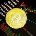 A gold Bitcoin coin rests on a screen displaying financial charts and graphs with various numbers and colored candlestick patterns. | MONEY6X