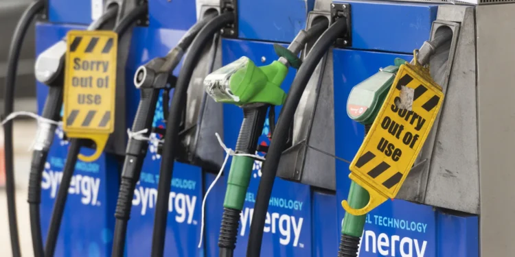 Four gas pumps at a station, with some nozzles covered by yellow “Sorry out of use” signs, indicating they are not available for fueling. The pumps are blue and display the word “synergy.”. | MONEY6X