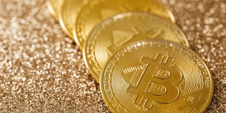 Five gold Bitcoin coins placed in a line on a shimmering, glittery golden surface. | MONEY6X